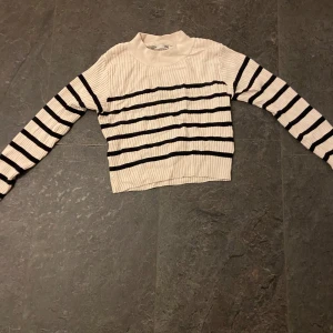 Randig ribbad tröja - Säljer en snygg randig tröja med ribbad struktur. Tröjan är vit med svarta ränder och har en croppad passform. Perfekt för en stilren look!
