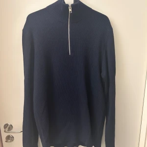 Mörkblå ribbad tröja med dragkedja - Snygg mörkblå tröja med ribbad struktur och halv dragkedja. Perfekt för kyligare dagar med sin långa ärmar och stilrena design. Passar bra till jeans för en avslappnad look.