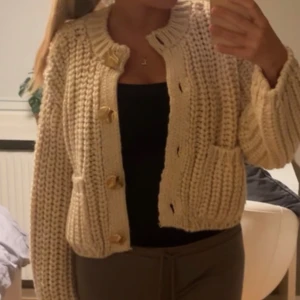 Beige stickad kofta med knappar - Mysig beige stickad kofta med stora knappar framtill. Perfekt för kyliga dagar och ger en avslappnad look.