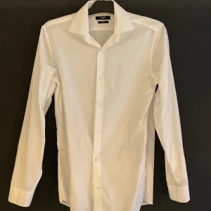 Vit kostym-skjorta från Jack & Jones - Snygg vit skjorta från Jack & Jones i slim fit. Perfekt att ha under kavaj eller tröja. Lite noppig på armbågarna och underarmarna.  Storlek S/40.