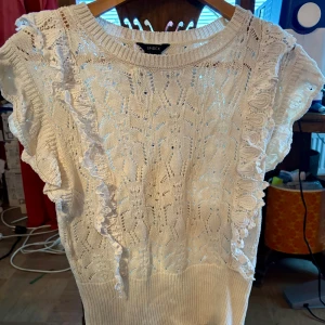 Vit spetsblus från Lindex - Säljer en söt vit spetsblus från Lindex med volangdetaljer längs ärmarna. Blusen har en vacker spetsdesign och är perfekt för en somrig look. Den är kortärmad och har en ribbad kant vid halsen.