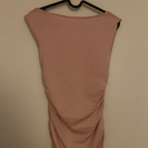 Rosa klänning med drapering - Elegant rosa klänning med draperad design och öppen rygg . Perfekt för en stilren look.