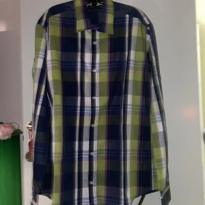 Ny skjorta från Tommy Hilfiger  - Snygg rutig skjorta från Tommy Hilfiger i grönt, blått och vitt. Skjortan har långa ärmar och kan vikas upp. Perfekt för en stilren look med en touch av färg.