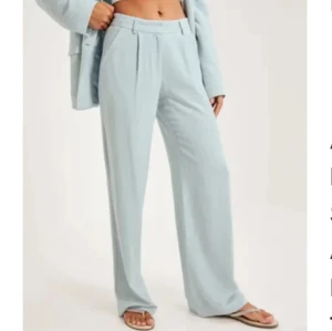 Ljusblå kostymbyxor från Nelly - Snygga ljusblå kostymbyxor från Nly trend med hög midja och vida ben. Perfekta för en stilren look. Byxorna har en klassisk design med veck framtill och bälteshällor.
