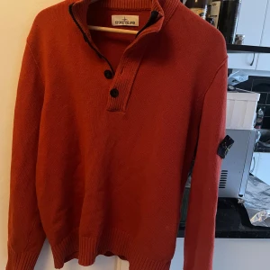 Rostfärgad tröja från Stone Island - Snygg rostfärgad tröja från Stone Island med ribbad krage och knappar framtill. Perfekt för kyligare dagar med sin stilrena design och långa ärmar.