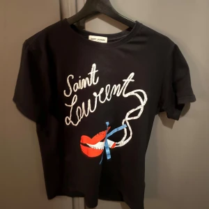 Svart t-shirt från Saint Laurent - Snygg svart t-shirt från Saint Laurent med ett coolt tryck av röda läppar och texten 'Saint Laurent' i vitt. Perfekt för en stilren look.
