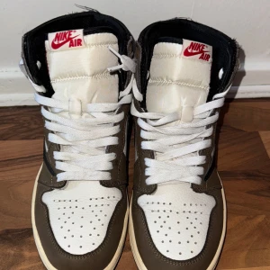 Nike Air Jordans i brunt och vitt - Snygga Nike Air Jordans i en stilren kombination av brunt och vitt med svarta detaljer. Skorna har klassisk snörning och perforerade detaljer på tån för extra ventilation. Perfekta för dig som vill ha en ikonisk sneaker med en modern twist.