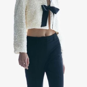 Vit paljettjacka med svarta rosetter - Snygg vit paljettjacka med två stora svarta rosetter framtill. Jackan är croppad och långärmad, perfekt för nyår. Helt oanvänd och slutsåld på hemsidan. Skriv privat för fler frågor💕