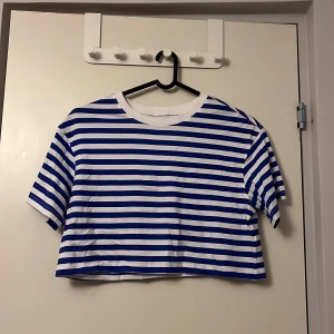 Randig croppad t-shirt från FSBN Sister - Säljer en blå- och vitrandig croppad t-shirt från FSBN Sister. Den har korta ärmar och en klassisk rund halsringning. Perfekt för en avslappnad stil.
