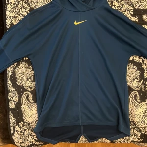 Blå hoodie från Nike - Snygg blå hoodie från Nike med gul logga på bröstet. Perfekt för en sportig look eller avslappnad stil. Den har en praktisk huva och är tillverkad i ett mjukt material.