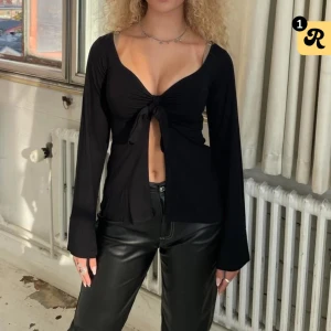 Svårt långärmad knyttopp - Trendig svart långärmad topp med knyt framtill. Perfekt för en stilren look. Använd fåtal gånger. 