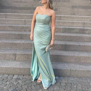 Glittrig mintgrön axelbandslös balklänning - Vacker glittrig mintgrön balklänning som endast är använd en gång! Köpt från Dressroom Linné, Orginalpris 3990kr. Sitter så smickrande och glittrar så fint i solen eller med blixt. Skimrar även i guld ibland som man kan se på några av bilderna. Inbyggd bh, och passar storlek 38. Jag är 166 cm lång och använder 7cm höga klackar i bilden  Den enda skavanken är lite BUS-rester på insidan. Knappt märkbart. Köper man klänningen får man även en matchande fluga som en eventuell baldejt kan ha! 