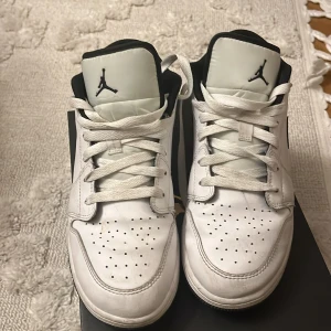 Vita och svarta Nike Air Jordans - Säljer ett par klassiska vita och svarta Nike Air Jordans med snörning. Skorna har en stilren design med perforerade detaljer på tån och den ikoniska Jumpman-loggan på plösen.