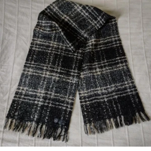 Svart/grå/beige/vit rutig stickad halsduk - made in France - Sjukt snygg svart/grå/beige/vit rutig lite lurvig halsduk med fransar. Made in France. Ca 150 cm lång exkl. fransarna och 30 cm bred. 73% Akryl 14% polyester 13% ull. Bara använd någon enstaka gång. 