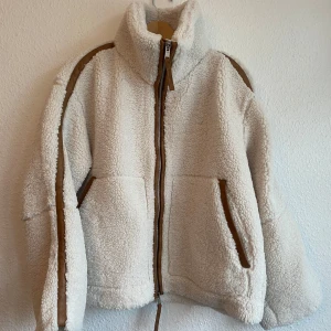 Ny cremevit teddyjacka i storlek XS från H&M - En cremvit tjock och varm teddyjacka i mjuk pile med kantband i ytbehandlad kvalitet. Jackan har lös passform, ståkrage, tvåvägsdragkedja fram och kängurufickor. Fodrad och lätt vadderad.  Storlek: XS ( oversized) HM