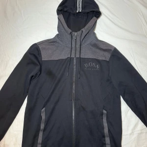 Svart och grå hoodie från Hugo Boss - Snygg och sällsynt Hugo Boss hoodie i riktigt bra skick, endast använd ett fåtal gånger. Storlek M men passar S-M. Tveka inte på att höra av dig ifall du har några frågor, jag svarar snabbt.