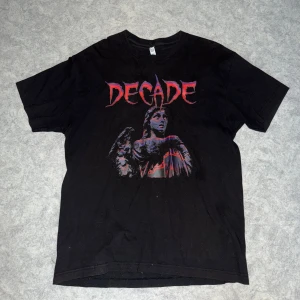 Svart t-shirt med tryck - Cool svart t-shirt med ett tryck av en ängel och texten 'DECADE' i rött. Perfekt för en avslappnad stil med en edgy touch.