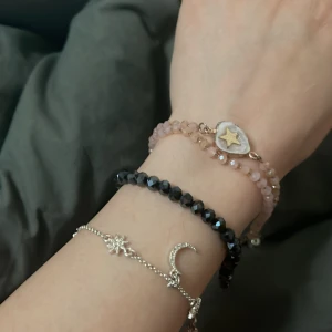 Set med tre armband i olika stilar - Säljer ett set med tre armband: ett silverfärgat med månar och stjärnor, ett svart glittrigt och ett rosa med en stjärndetalj. Perfekt för att mixa och matcha!Varje sort kostar 50 kr men alla kostar 130