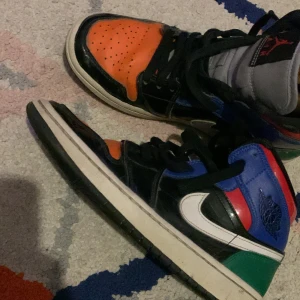 Flerfärgade Nike Air Jordans - Säljer ett par unika Nike Air Jordans i flera färger: orange, blå, grön, röd och svart. Skorna har klassisk snörning och en vit sula. Perfekta för dig som vill sticka ut med en färgglad stil.