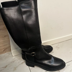 Svarta stövlar med dragkedja - Snygga svarta stövlar i skinn med dragkedja och dekorativt spänne. Perfekta för höst och vinter.