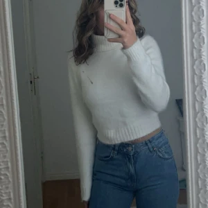 Vit stickad polotröja - Säljer en mysig vit stickad polotröja med långa ärmar. Perfekt för kyligare dagar och passar bra till jeans eller kjol. Tröjan har en klassisk design med ribbstickade muddar vid ärmslut och nederkant.