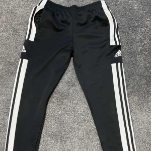Svarta träningsbyxor från Adidas - Snygga svarta träningsbyxor från Adidas med klassiska vita ränder längs sidorna. Dom har dragkedjor vid benen. Byxorna är köpta från Intersport. Dom är i mycket bra skick och är använda 1-2 gånger. Storlek på dom är 164 (junior storlek) XS/34 i vuxenstorlek. 