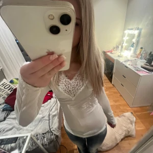 Vit långärmad topp med spetsdetaljer - Säljer en stilren vit långärmad topp med vacker spetsdetalj vid halsringningen. Perfekt för en elegant look. Passar bra till både jeans och kjol.