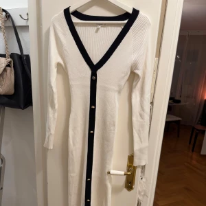 Vit ribbad klänning från Missguided - Snygg vit ribbad klänning från Missguided med svarta detaljer och knappar framtill. Klänningen har en v-ringad design och långa ärmar. Saknas en knapp. 
