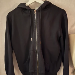 Svart hoodie med dragkedja - Säljer en klassisk svart hoodie med dragkedja och huva. Tröjan har långa ärmar och en bekväm passform. Perfekt för en avslappnad stil.