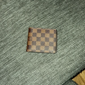 Brun rutig plånbok - Snygg brun plånbok med klassiskt rutigt mönster. Perfekt för att hålla ordning på kort och kontanter. Kompakt och stilren design som passar i fickan.