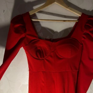 Röd klänning med puffärmar - Snygg röd klänning med puffärmar och markerad byst. Perfekt för en kväll ute eller en speciell tillställning. Klänningen har en elegant passform och en djup urringning. Endast använd en gång