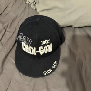 Svart keps med broderad text - Snygg svart keps med broderad text 'CHIN-GON' i vitt och grått. Perfekt för en avslappnad stil.