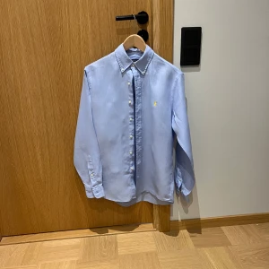 Ljusblå linneskjorta Ralph lauren - Säljer denna ljusblå linneskjorta från Ralph Lauren. Köpt i sommars i Spanien. Använd någon enstaka gång. Är i nyskick utan några defekter. Nypris 1750