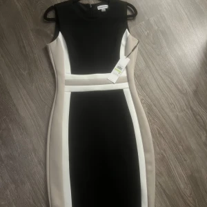 Svart och beige klänning från Calvin Klein - Elegant cocktailklänning från Calvin klein oanvänd med prislappar kvar! Tror det är storlek 34-36. Dragkedja där bak att stänga klänningen