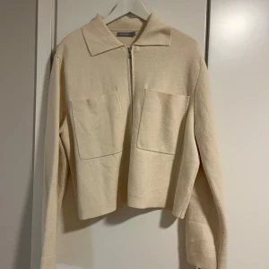 Beige jacka med dragkedja - Snygg beige jacka från Åhléns med dragkedja framtill och två stora fickor. Jackan har en krage och långa ärmar, perfekt för en stilren look.