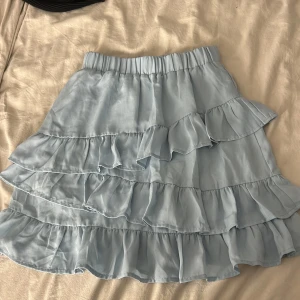 Ljusblå volangkjol från NA-KD - Säljer en söt ljusblå volangkjol från NA-KD. Kjolen har flera lager av volanger och en elastisk midja för en bekväm passform. Perfekt för en somrig look! 💙