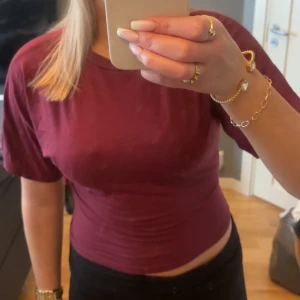 Vinröd t-shirt - Säljer en enkel och stilren vinröd t-shirt med korta ärmar. Ärmarna är utsvängda med en tajt midja.