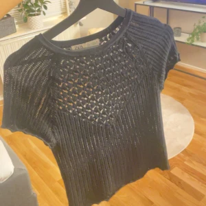 Svart stickad topp från Zara - Snygg svart stickad topp från Zara med ett unikt mönster på framsidan. Toppen har korta ärmar och en rund halsringning. Perfekt för fest men även vardag!