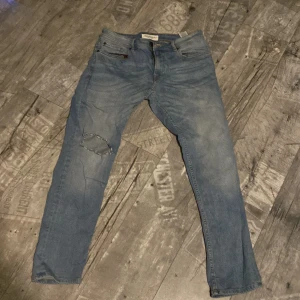 Blå jeans från Stock & Hank - Snygga blå jeans från Stock & Hank med en klassisk femficksdesign. De har en dragkedja och knapp framtill samt en liten reva på ena benet för en trendig look. Perfekta för en avslappnad stil.