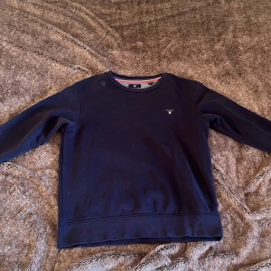 Mörkblå tröja från GANT - Säljer en stilren mörkblå tröja från GANT med rund halsringning och diskret logga på bröstet. Perfekt för en avslappnad och snygg look. Tröjan har långa ärmar och ribbade muddar. Den har inga skador eller håll 