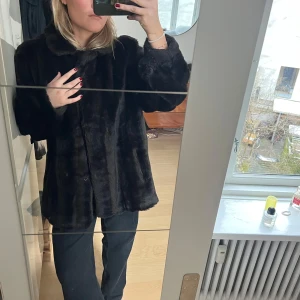 Svart/ brun pälsjacka - Snygg svart pälsjacka med knappar framtill. Perfekt för att hålla sig varm och stilren under kyliga dagar. Jackan har en klassisk design med långa ärmar och en mjuk känsla.