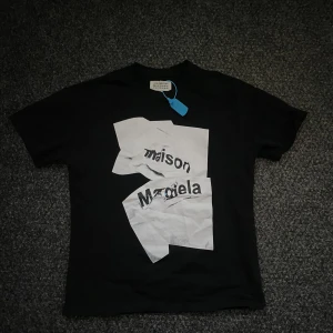 Svart t-shirt från Maison Margiela - Snygg svart t-shirt från Maison Margiela med ett unikt tryck i vitt på framsidan. Perfekt för en stilren look. T-shirten har korta ärmar och en klassisk passform.