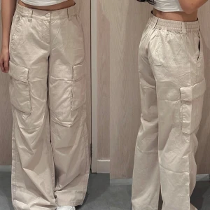 Beige cargopants - Snygga beige cargopants med hög midja och loose fit. Byxorna har stora fickor på sidorna och en knappstängning framtill. Perfekta för en avslappnad stil.