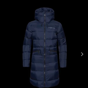 Mörkblå dunjacka från Sail Racing - Snygg och varm mörkblå dunjacka från Sail Racin - Spray Down Parka W. Jackan har en lång modell med huva och dragkedja framtill. Perfekt för kalla dagar med sin pufferdesign och praktiska fickor med dragkedjor. Ordpris 4 500 kr.