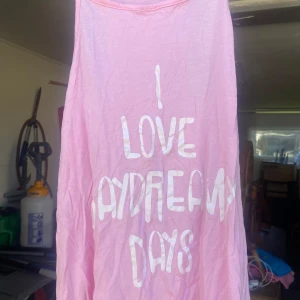 Rosa linne från Skill Summer Vibes - Säljer ett supergulligt rosa linne från Skill Summer Vibes med texten 'I Love Daydream Days' i vitt. Perfekt för varma sommardagar! Det är ärmlöst och har en avslappnad passform.