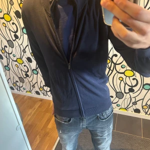 Mörkblå kofta från John Henric - Säljer en snygg och stilren mörkblå kofta från John Henric. Den har en dragkedja framtill och är perfekt för både vardag och lite finare tillfällen. Koftan är i bra skick och passar perfekt till jeans eller chinos. Perfekt för höst och vår!