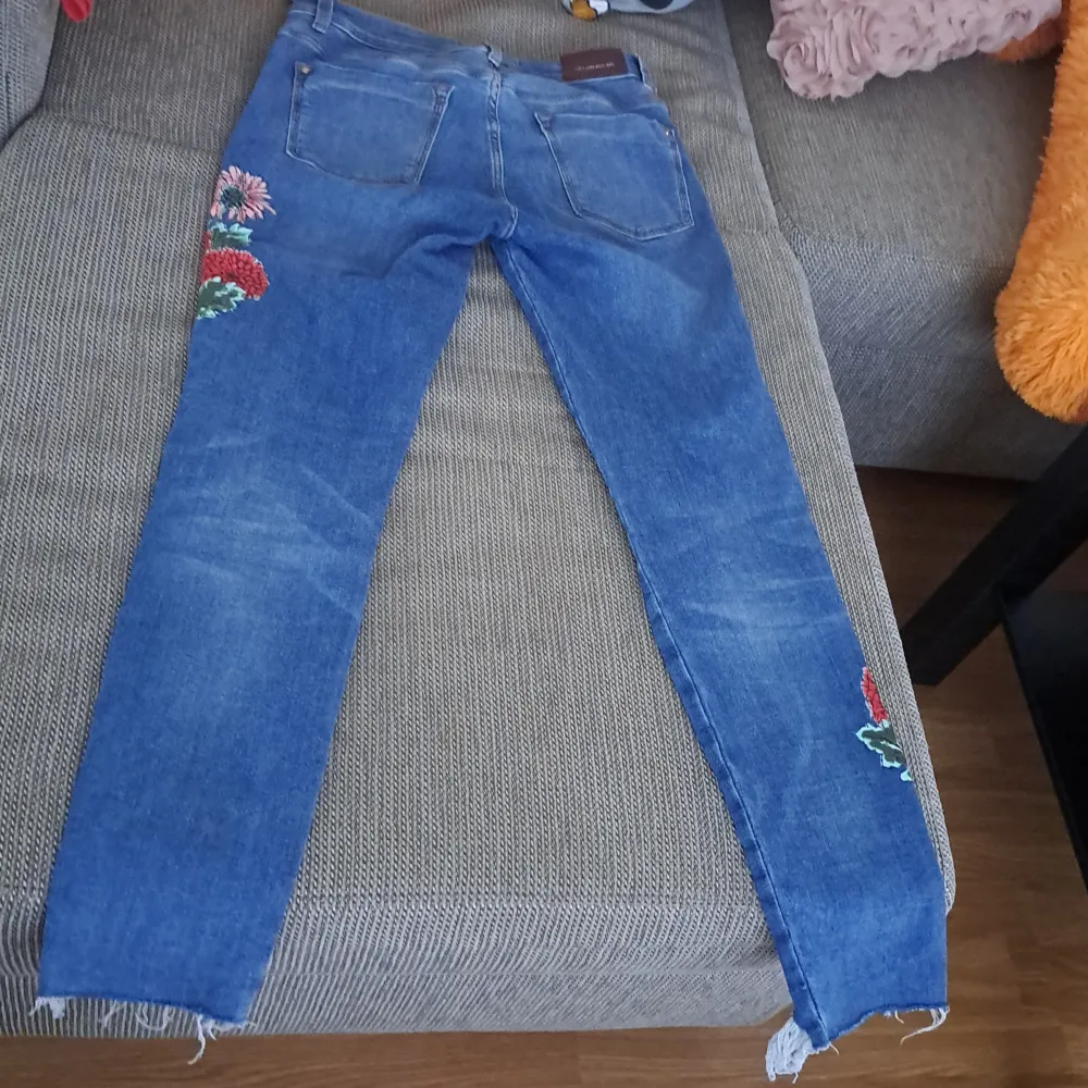 Säljer ett par snygga blå jeans med blommigt broderi på benen. De har en skinny passform och är i ett välanvänt skick. Perfekta för en casual look med en twist! De har en klassisk femficksdesign och en dragkedja med knapp framtill.. Jeans & Byxor.