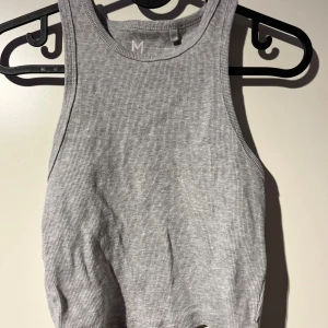 Grå ribbad linnetopp - Säljer en stilren grå ribbad linnetopp i storlek M. Perfekt för sommardagar eller som ett lager under en jacka. Toppen är ärmlös och har en tight passform som framhäver figuren. Superbekväm och lätt att matcha med olika outfits!