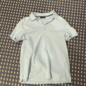 Ljusblå pikétröja från J. Lindeberg - Snygg ljusblå pikétröja från J. Lindeberg med klassisk krage och korta ärmar. avslappnad och stilren. Passar bra till både jeans och shorts.