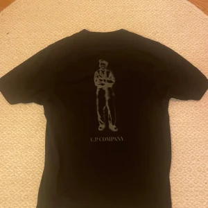 Svart t-shirt från C.P. Company - Snygg svart t-shirt från C.P. Company med ett  tryck på både fram- och baksidan. Köpt från NK med nypris på 1000kr+. T-shirten är lite tjockare i materialet och man skulle väl kunna säga att den är lite oversized i passformen. 500kr för en snabb affär